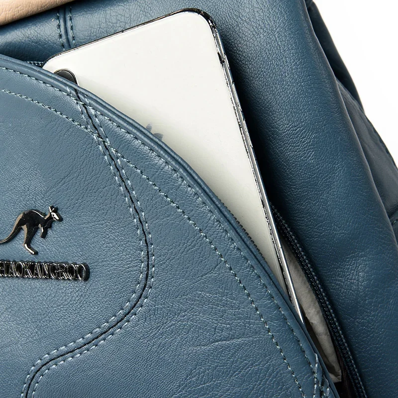 Close-up of a teal leather backpack with a phone in a zippered pocket. The backpack has stitching detail and a kangaroo logo.