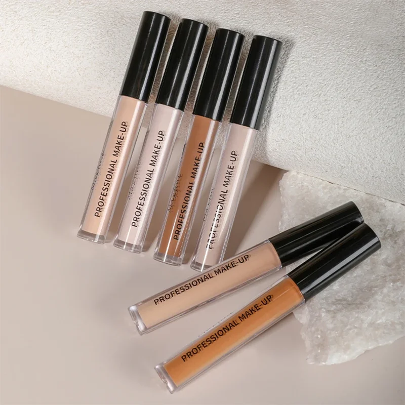 Close-up view of several tubes of concealer in various shades of beige and tan, arranged on a light beige surface. Each tube features the text 'PROFESSIONAL MAKE-UP' printed on the side.