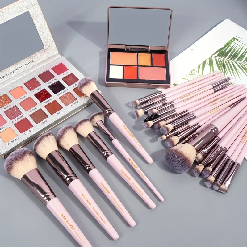 A collection of pink makeup brushes and palettes arranged on a gray surface. The brushes are arranged in a fan shape, with the handles pointing towards the center. The palettes are a mix of eyeshadow and blush colors. The overall aesthetic is feminine and luxurious.