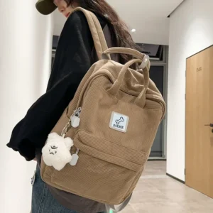 A tan corduroy backpack with a small white plush toy attached to it. The backpack has a small white patch with the word "DIEHE" on it.