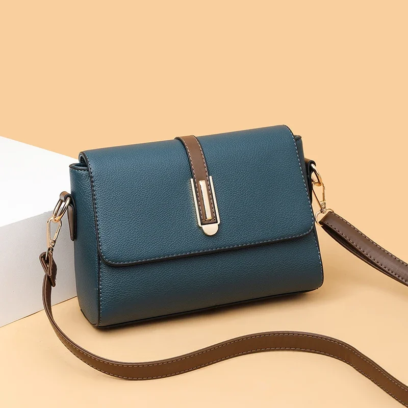 A teal and brown crossbody bag sits on a beige surface. The bag is made of leather and has a gold clasp.