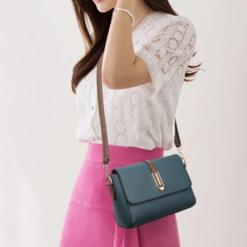 A woman is shown from the waist up, wearing a white lace blouse and a pink skirt. She has a teal crossbody bag slung across her body. The bag has a gold clasp and a brown strap. The image is a product shot, likely for an online store.