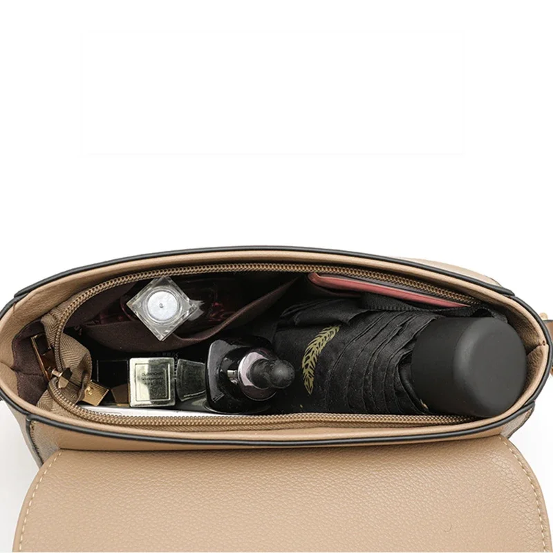 A beige handbag is shown open, revealing its contents: a black umbrella, a small bottle of perfume, a compact, and a phone. The bag is made of a soft, supple leather-like material, and the zipper is visible at the top.