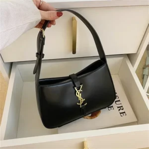 A black handbag with a gold YSL logo sits in a drawer.