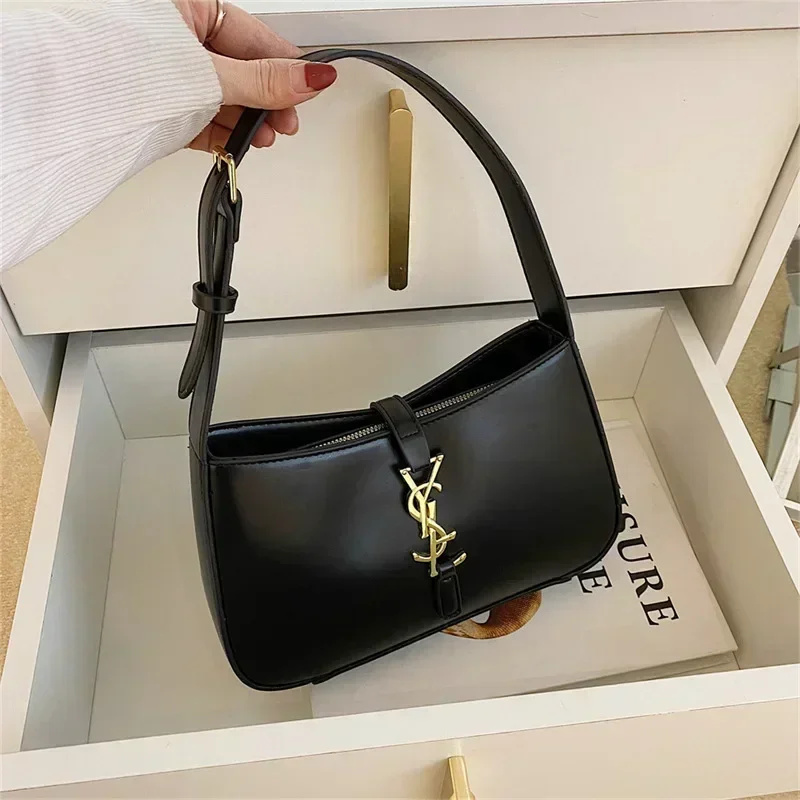 A black shoulder bag with a gold YSL logo sits in a white drawer.