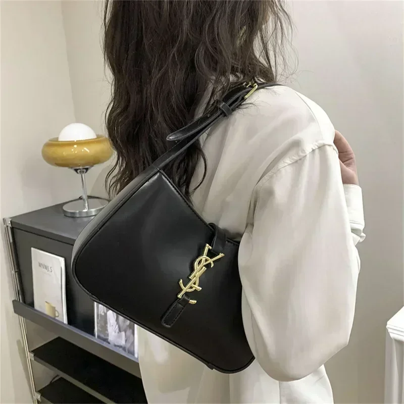 A woman with long black hair is wearing a white shirt and a black shoulder bag with a gold logo. The bag is a half-moon shape and is worn across the body.