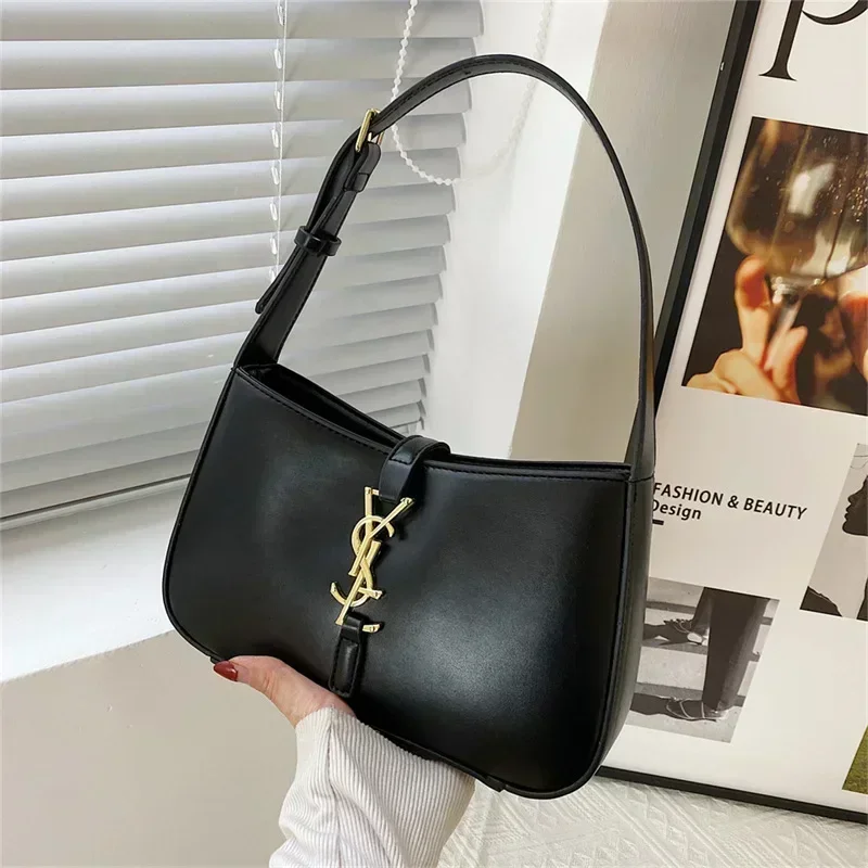 A black handbag with a gold YSL logo is shown in the image. The bag is a half-moon shape and has a short strap. The bag is being held by a hand.