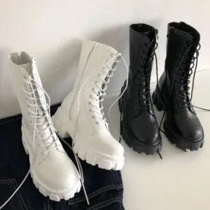 Three pairs of platform lace-up boots in white and black. Two pairs are white and one pair is black. They are arranged on a light-grey surface and partly on a pair of jeans.