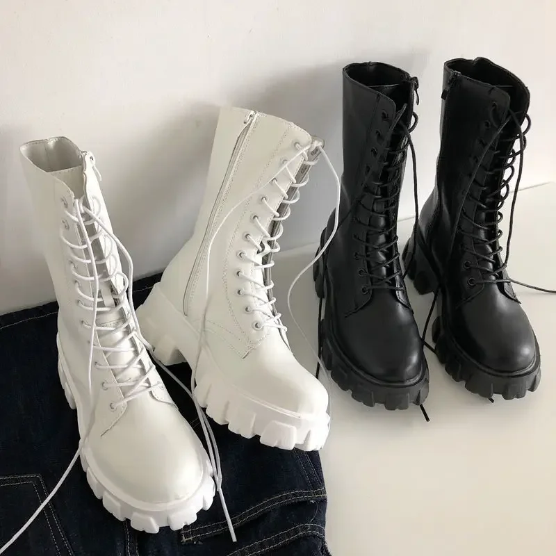 Close-up view of three pairs of chunky lace-up boots. Two pairs are white and one pair is black. The boots are positioned on a surface, partially covered by dark-colored denim.