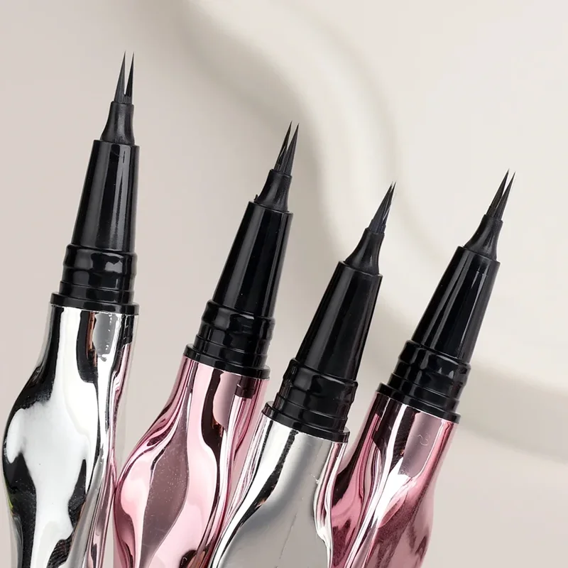 Close-up view of four eyeliner pens with sleek, curved metallic bodies in silver and rose gold. The brush tips are fine and black.