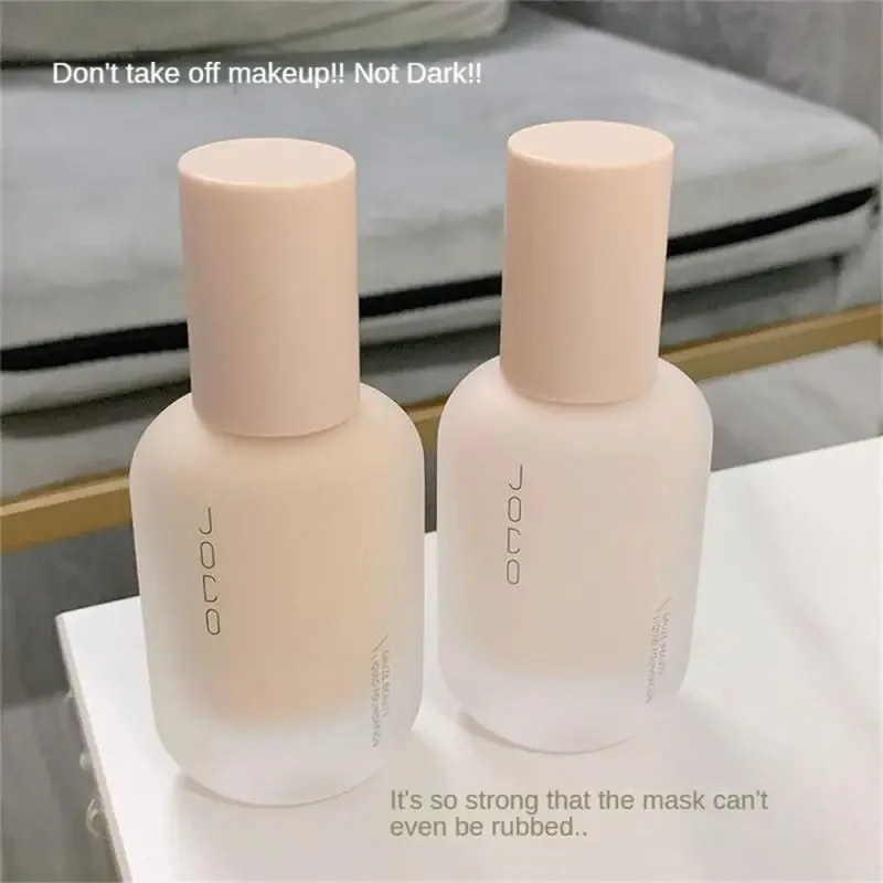 Two bottles of JOCO Liquid Foundation sit on a white surface. The bottles are light beige with a frosted finish and the brand name is printed on them. Text overlayed on the image reads: "Don't take off makeup!! Not Dark!!" and "It's so strong that the mask can't even be rubbed.."