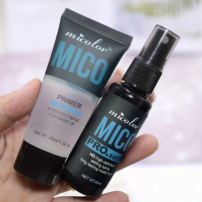 Close-up view of a hand holding two MICO brand makeup products: a primer tube and a setting spray bottle. Both products feature a sleek black design with blue accents and showcase their respective uses and weights.