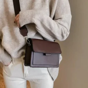 A person wearing a light gray sweater and white pants is carrying a brown rectangular crossbody bag.