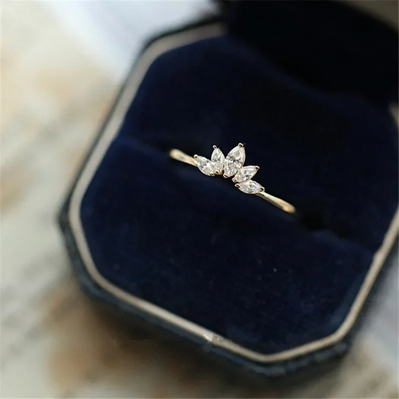 A gold ring with small, clear stones set in a marquise shape sits in a dark blue velvet ring box.