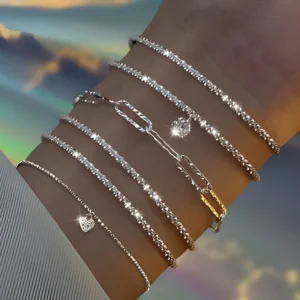 Close-up of a woman's wrist adorned with a stack of delicate silver bracelets, each featuring unique charms and textures. The bracelets are layered in varying lengths and styles, creating a stylish and eye-catching accessory.