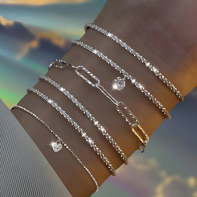 Close-up of a woman's wrist adorned with a stack of delicate silver bracelets, each featuring a unique design. The bracelets are layered, creating a stylish and eye-catching look. The background is a soft, pastel sky with a dreamy, ethereal quality, enhancing the overall aesthetic.