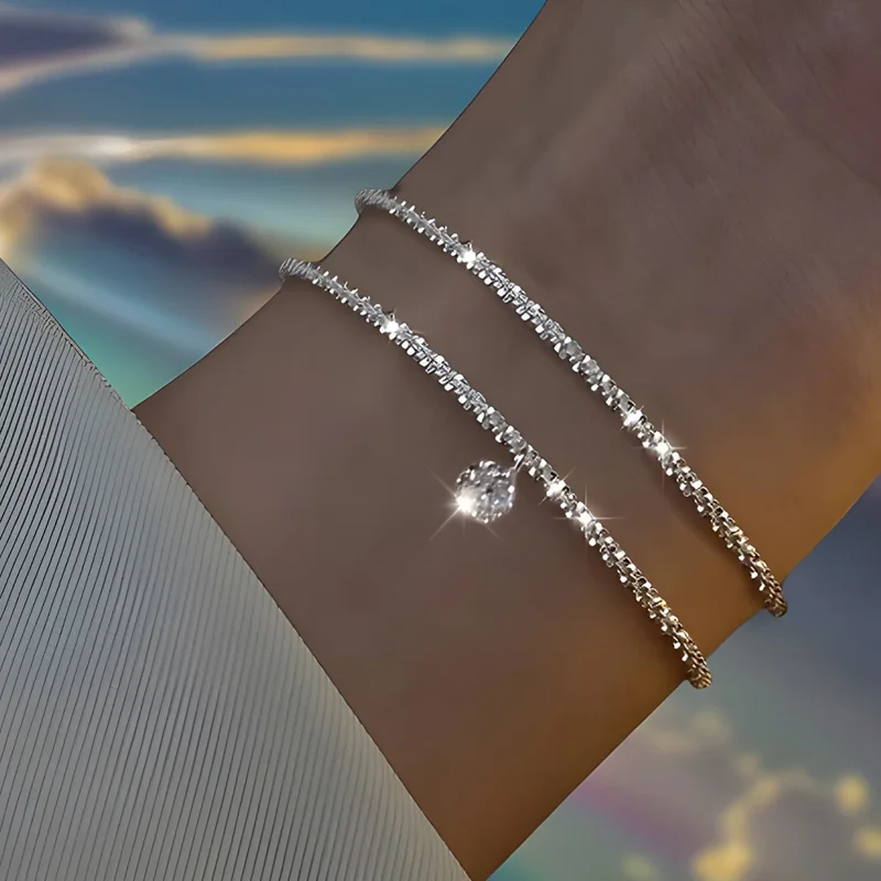 Close-up of a woman's wrist adorned with two delicate silver bracelets. The bracelets are intricately designed with small, sparkling stones and feature a single, larger stone pendant.