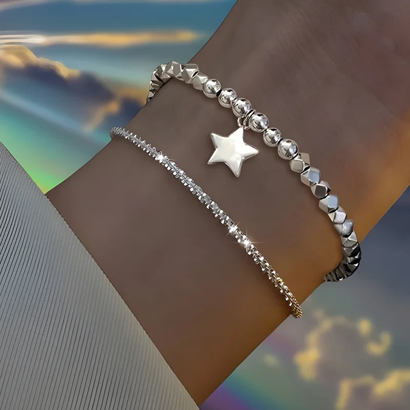 Close-up of a woman's wrist wearing two silver bracelets. One bracelet is made of small, faceted beads, and the other is a delicate chain with a star charm.
