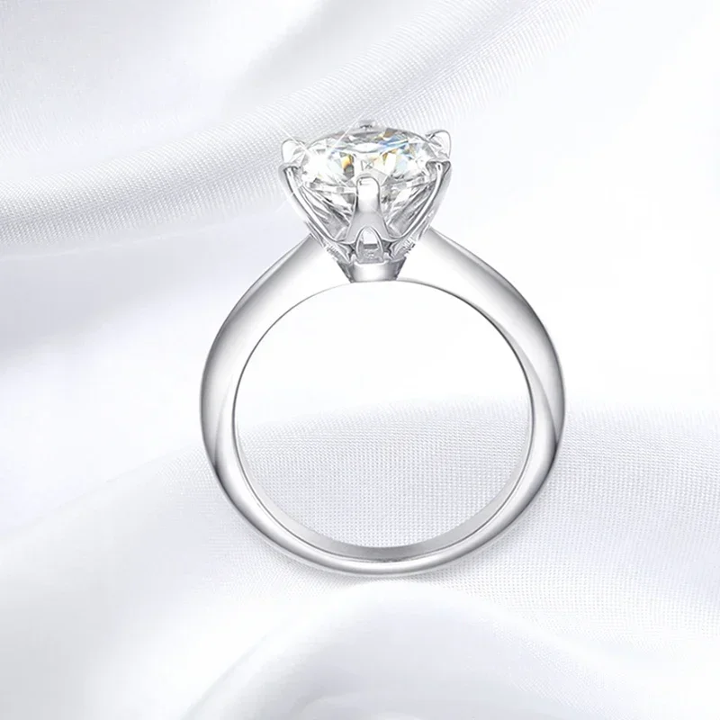 A solitaire diamond engagement ring sits on a white satin fabric.