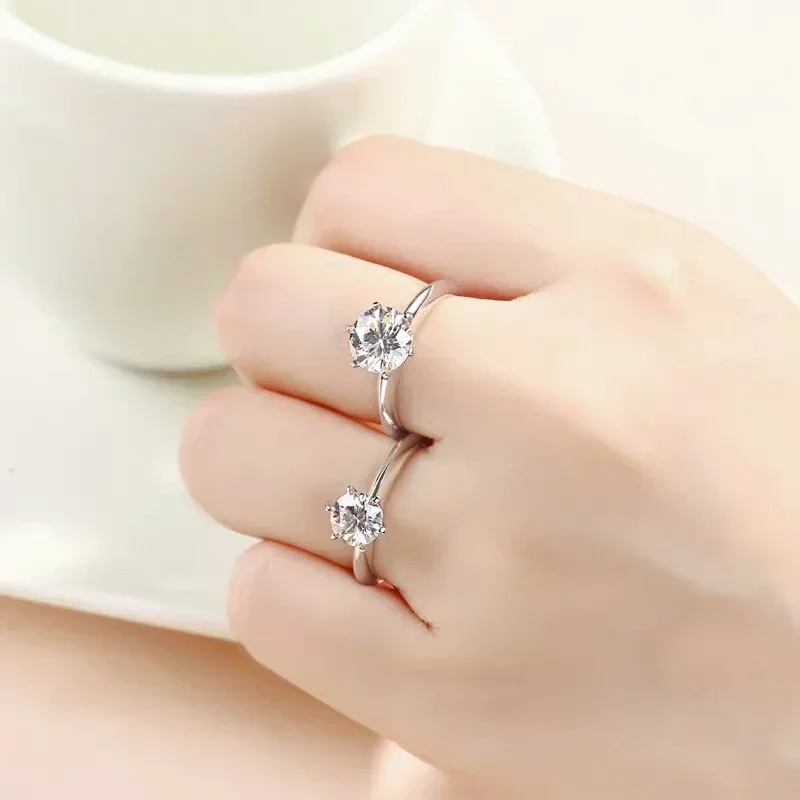 Close-up of a woman's hand wearing two solitaire diamond rings. The rings are simple and elegant, with a single round brilliant-cut diamond set in a four-prong setting. The diamonds sparkle beautifully, and the rings are a perfect complement to the woman's fair skin. The image is set against a soft, white background, which enhances the sparkle of the diamonds.