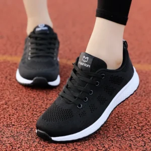 Close-up of a woman's feet wearing a pair of black breathable mesh sneakers with white soles. The shoes have a simple design and the word "Fashion" is subtly printed on the side.
