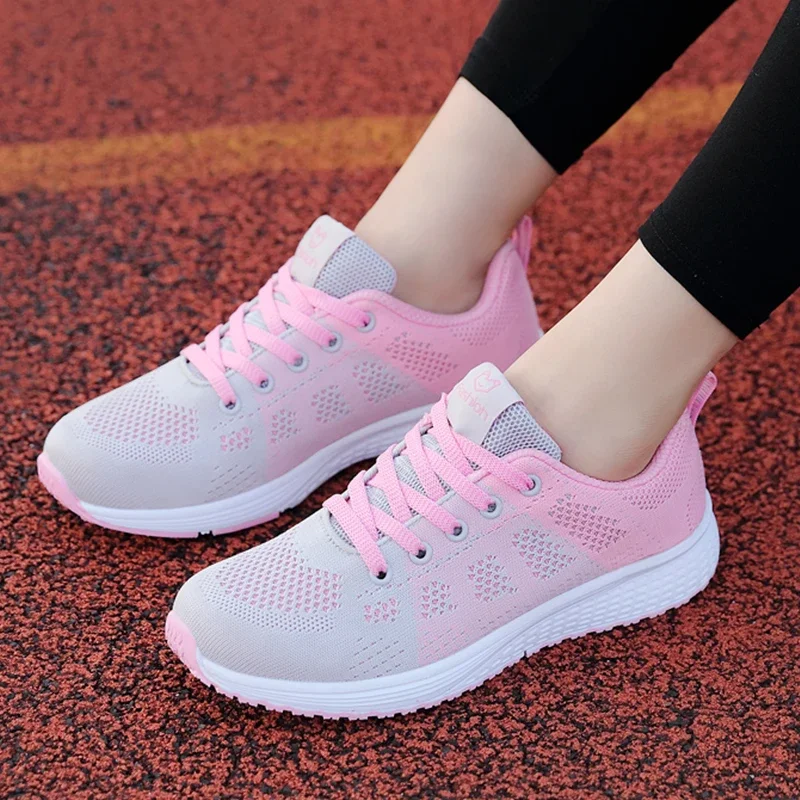 A pair of pink and grey women's sneakers on a red track.