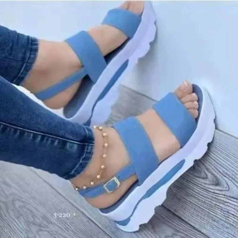 A pair of light blue platform sandals with white soles. The sandals are worn by a person wearing jeans. The sandals have two straps across the foot and a buckle closure.