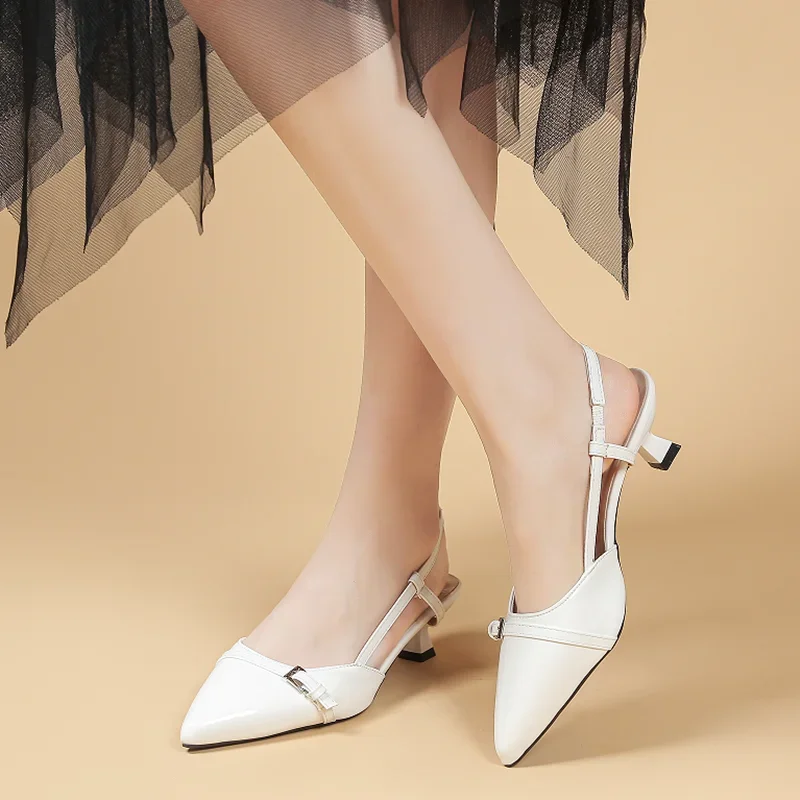 A pair of white slingback heels with a pointed toe and a low kitten heel. The shoes are worn by a woman who is wearing a black tulle skirt.