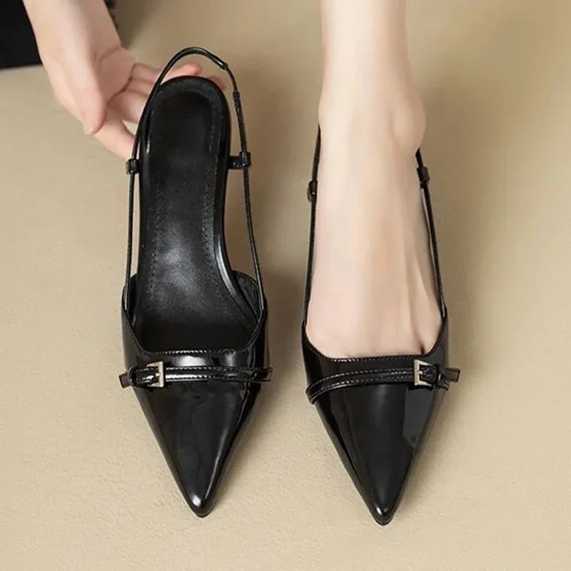 A pair of black patent leather pumps with a slingback design and a small buckle detail. The shoes are pointed-toe and have a low heel.