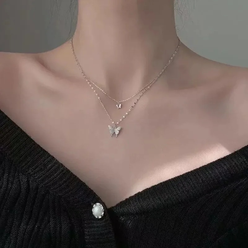 A close-up shot of a woman wearing a delicate layered necklace featuring two butterfly pendants. The necklace is made of a thin chain and the butterflies are small and adorned with sparkling stones.