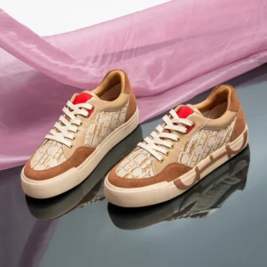 A pair of beige and brown sneakers with red accents sits on a reflective surface, partially covered by a sheer pink fabric.