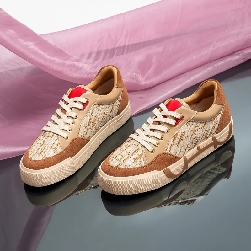A pair of beige and brown sneakers with red accents sits on a reflective surface, partially covered by a sheer pink fabric.