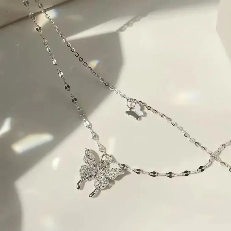 Close-up of a delicate silver necklace with two butterfly pendants adorned with sparkling crystals, resting on a soft, light background.