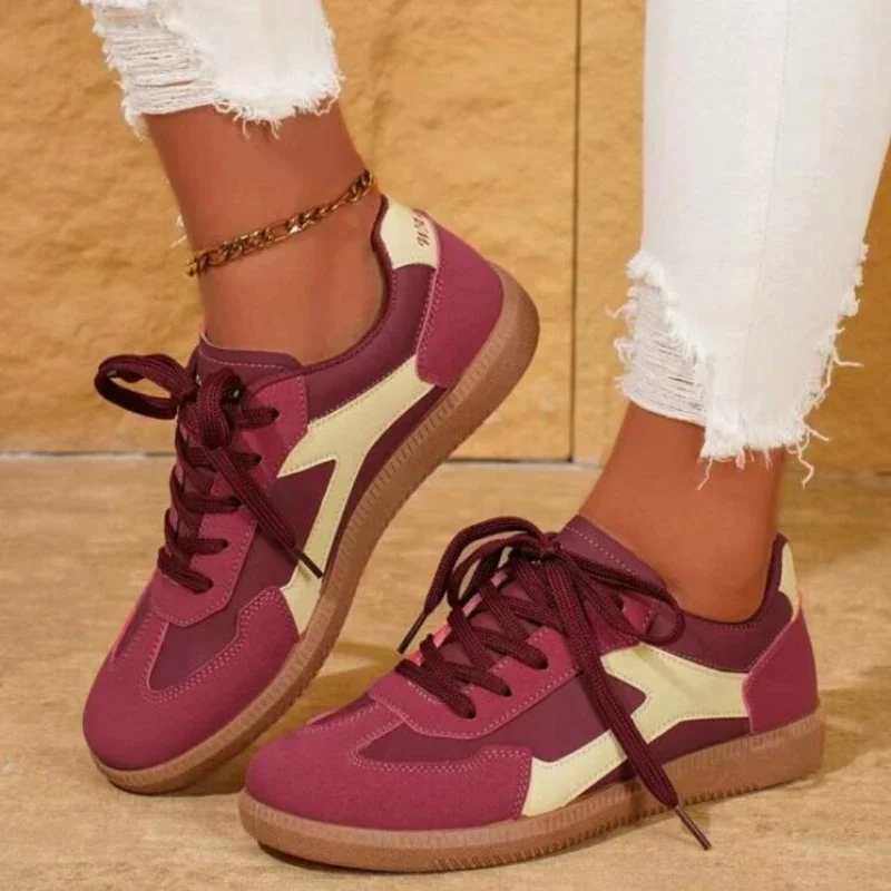 A pair of burgundy and cream sneakers with brown soles. The sneakers are lace-up and have a casual style. The model is wearing white jeans.
