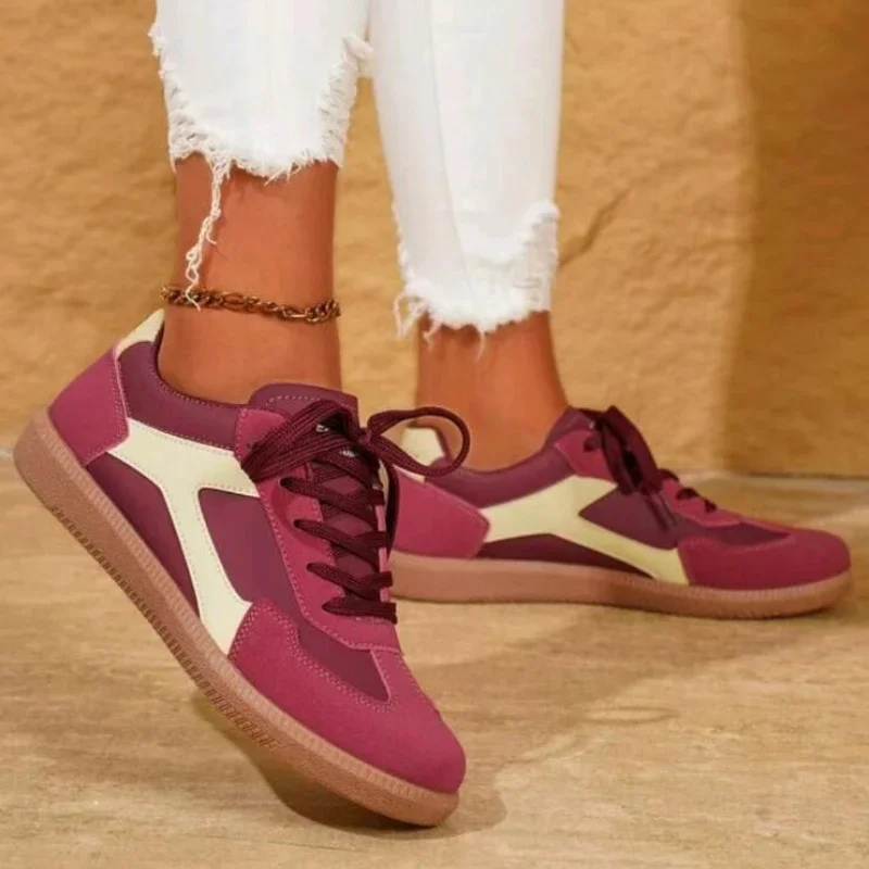 A close-up shot of a woman's feet wearing a pair of burgundy and cream colored sneakers. The sneakers are lace-up and have a chunky sole. The woman is wearing white jeans.