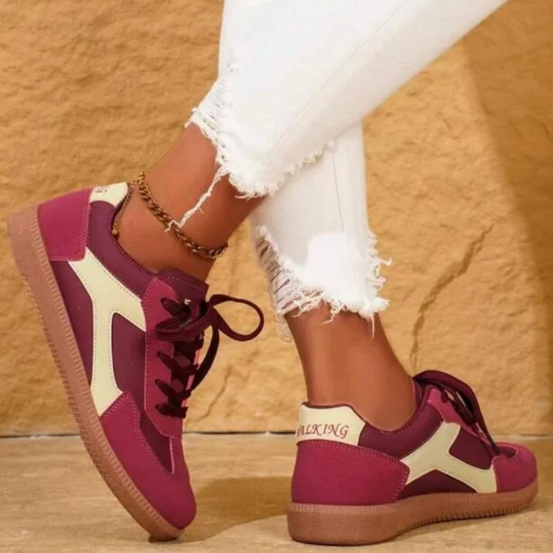 Close-up of a woman's feet wearing a pair of maroon and cream colored sneakers. The sneakers are lace-up and have a chunky sole. The woman is wearing white jeans.