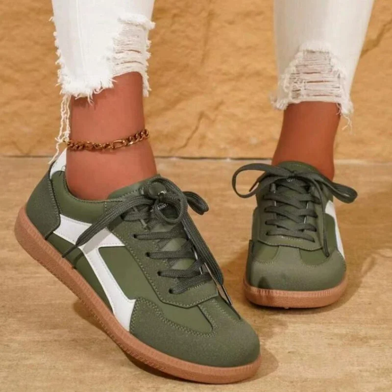 A pair of olive green and white sneakers with a gum sole. The sneakers are worn by a model who is wearing white ripped jeans.