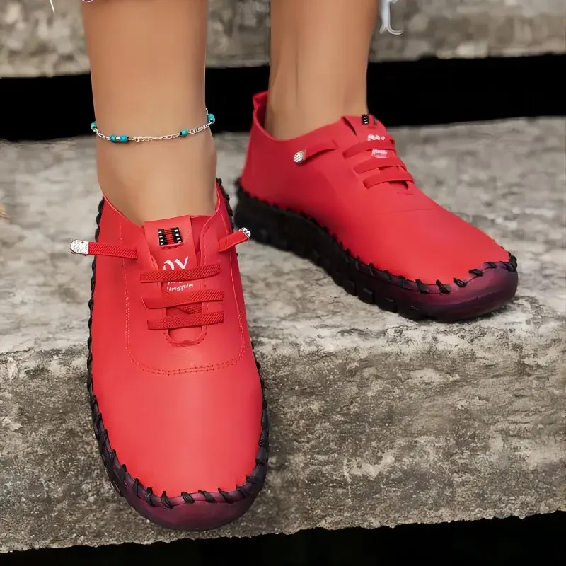 A pair of red women's shoes with black soles and laces. The shoes are on a woman's feet and are resting on a stone surface.
