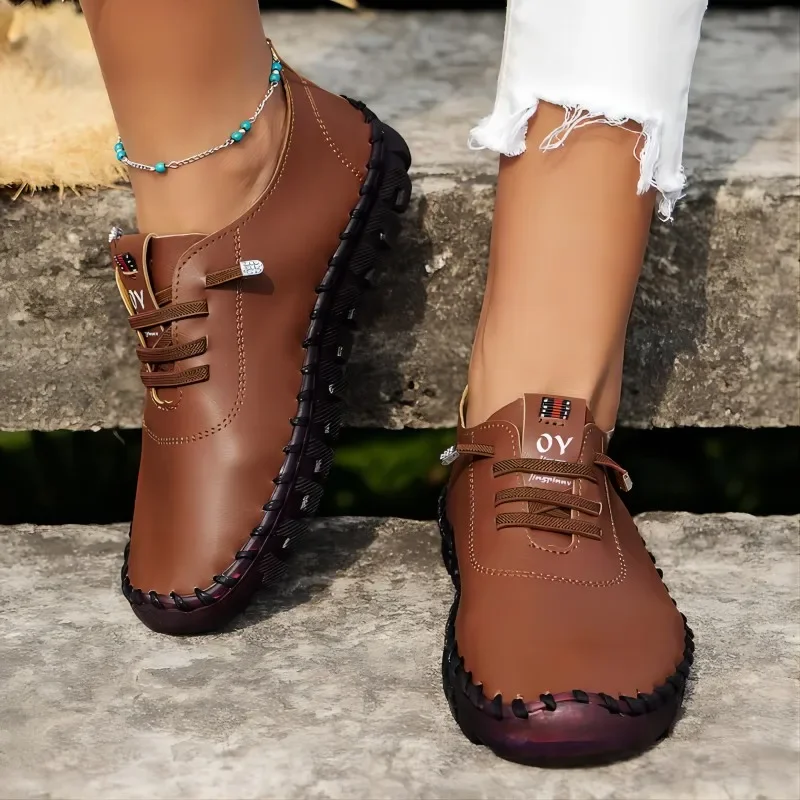 A pair of brown leather shoes with decorative stitching and laces. The shoes are worn by a person with their legs crossed.