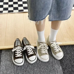 A person is wearing two pairs of canvas shoes. One pair is leopard print and the other pair is beige. The person is wearing white socks and a denim skirt.