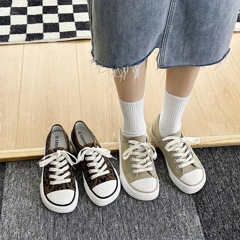 A person is wearing two pairs of canvas shoes. One pair is leopard print and the other pair is beige. The person is wearing white socks and a denim skirt.