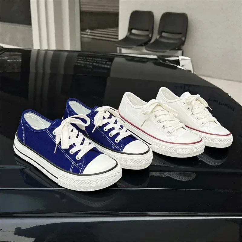 A pair of navy blue canvas sneakers and a pair of white canvas sneakers sit on a black surface. The sneakers are low-top and have white laces.