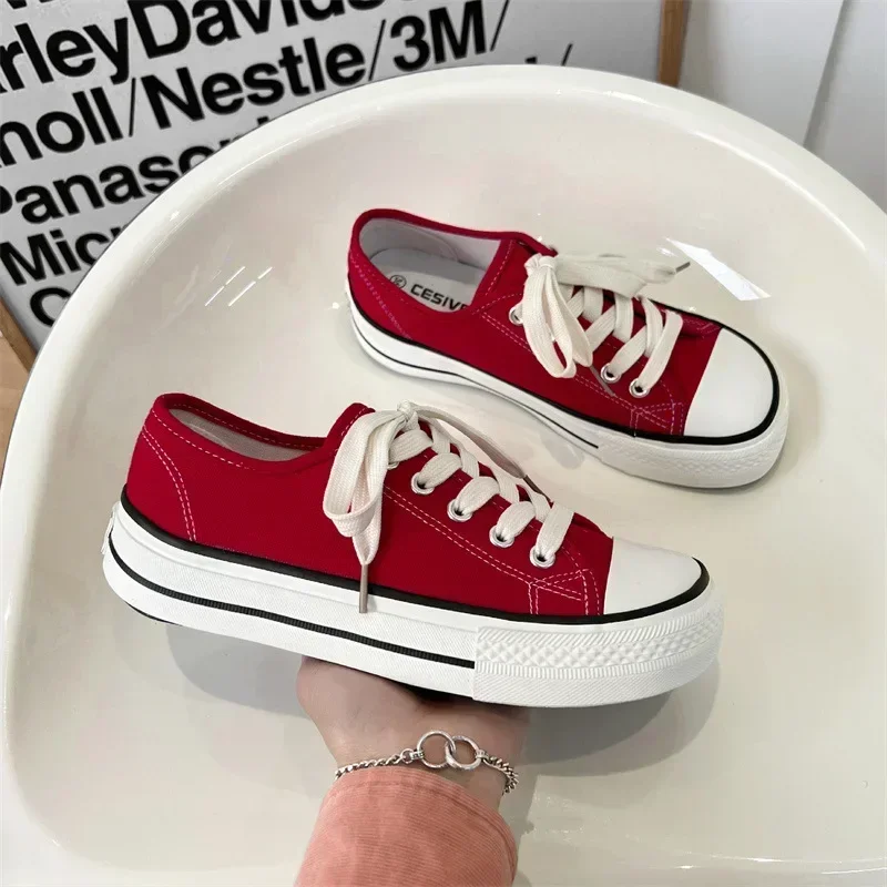 A pair of red canvas shoes with white soles and laces sits on a white surface. A person's hand holds one of the shoes.