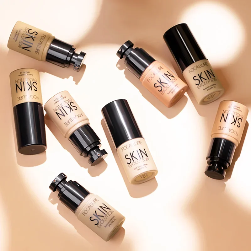 Multiple bottles of FOCALLURE Skin Evolution foundation are arranged on a beige surface. The bottles are various shades of beige and feature a black cap.