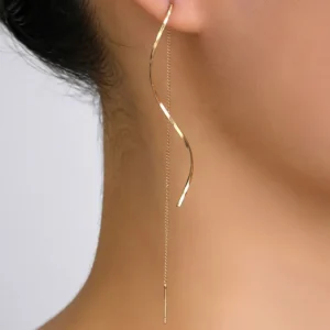 Close-up of a woman's ear adorned with a long, gold, twisted earring that hangs down to her neck.
