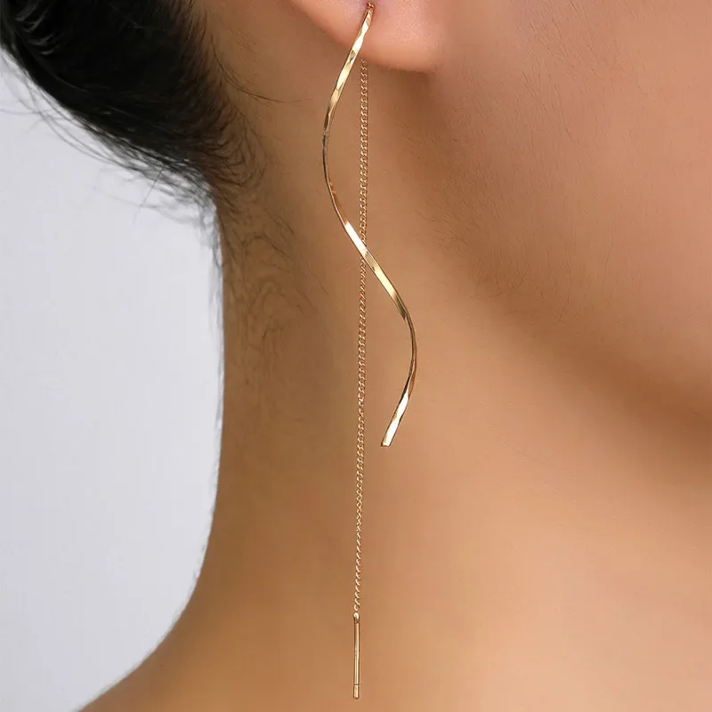 Close-up of a woman's ear wearing a long, gold, twisted earring that hangs down to her shoulder.