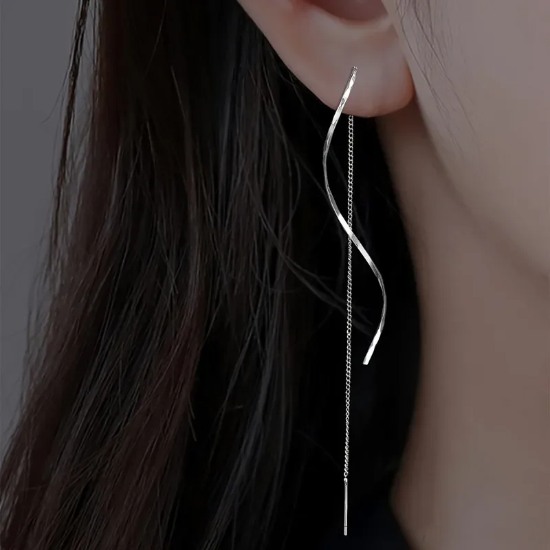 A close-up shot of a woman's ear with a long, silver dangling earring. The earring is twisted and features a delicate chain.