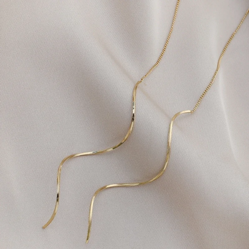 A pair of gold earrings with a wavy design rests on a beige fabric background.