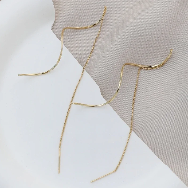 A pair of gold earrings with a wavy design and long chains.