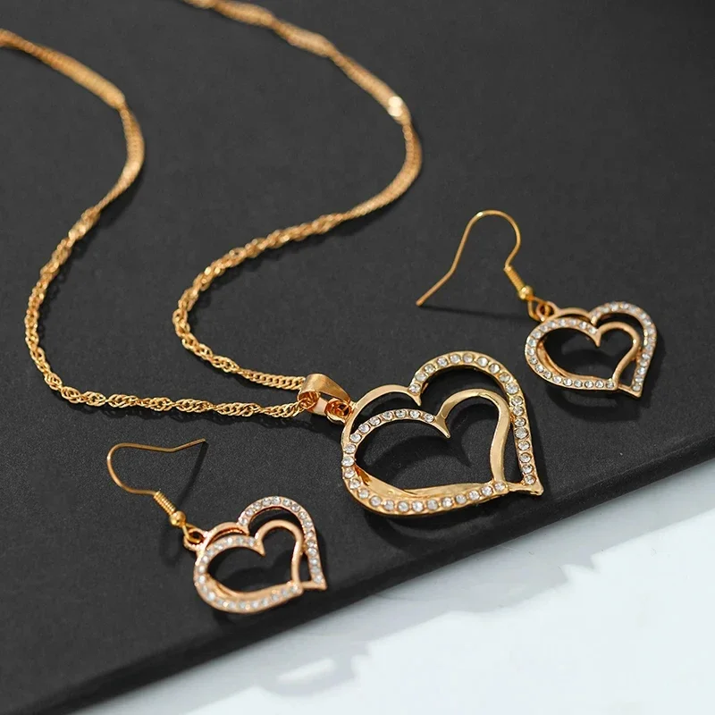 Gold necklace and earrings set with heart-shaped pendants adorned with sparkling crystals.